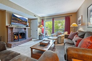 Un salon avec une cheminée, un téléviseur, un canapé et un balcon avec des rideaux.