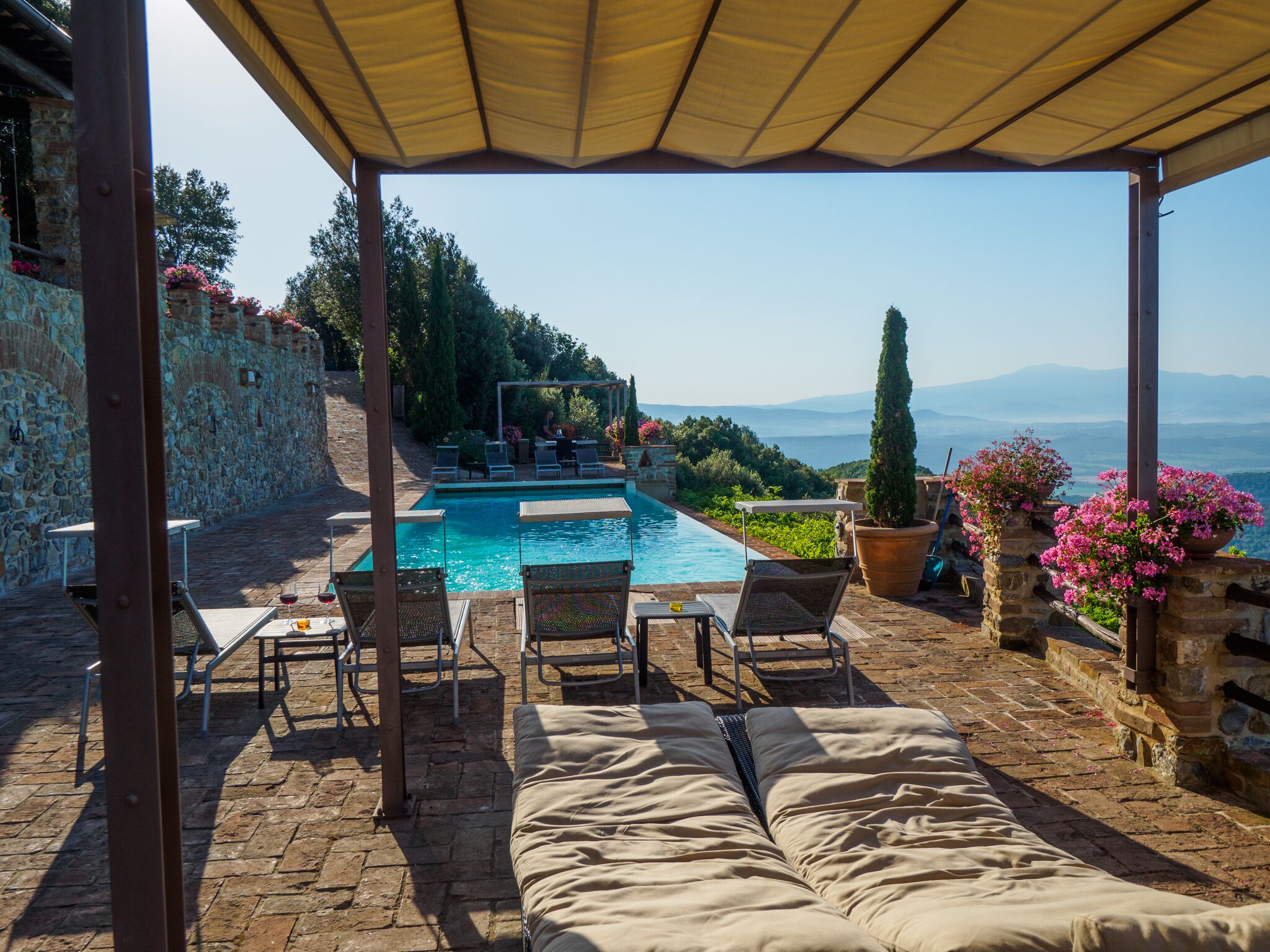 Ein Poolbereich mit Liegestühlen, einer überdachten Sitzgruppe und Blick auf die Berge.