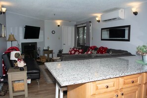 A modern living room with a fireplace, a flat-screen TV, and a kitchen island. - Winterplace E101 Condo Ski In Ski Out First Floor (Ghent)