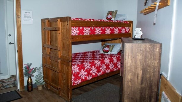 Ein Stockbett mit rotem und weißem Schneemuster, ein Holztisch und eine kleine Weihnachtstanne.