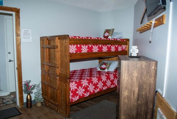 A bunk bed with a red and white snowflake pattern, a wooden desk, and a small Christmas tree.