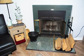 A room with a fireplace, a black leather sofa, a small Christmas tree, and a basket on a wooden cabinet.