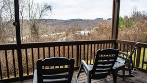 Ein überdachter Außenbereich mit zwei Schaukelstühlen und einem Tisch, mit Blick auf eine natürliche Landschaft.