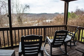 A covered outdoor area with two rocking chairs and a table, overlooking a natural landscape.