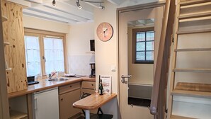 Een kleine keuken met een houten aanrecht, een spoelbak, een eettafel met een stoel en een klok aan de muur.