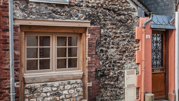 Een smalle straat met een stenen gebouw, voorzien van een houten raam en een metalen poort.