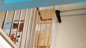 Een houten trap met een leuning, die uitkomt op een plateau met een witte muur en een houten kast.
