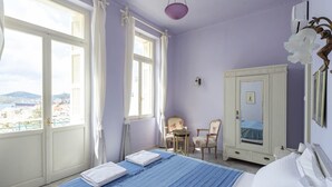 Un dormitori amb un llit, un armari, una cadira, una taula petita i una finestra amb cortines.