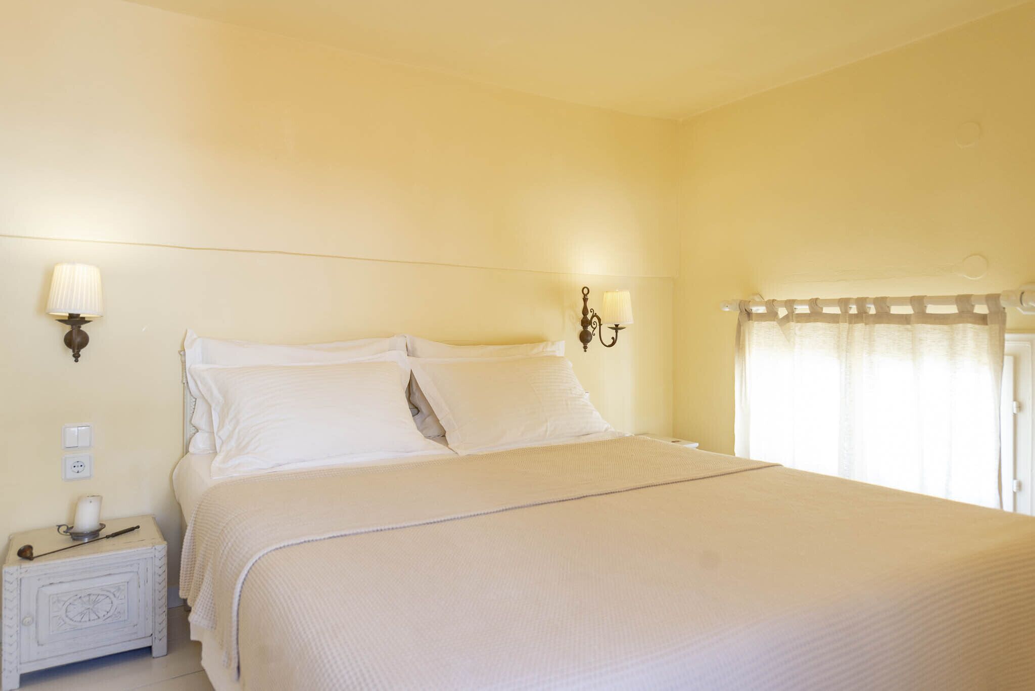 Un lit bien fait, avec du linge de lit blanc, une table de chevet avec une lampe et un luminaire fixé au mur.