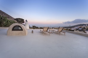 A rooftop terrace with two lounge chairs, a small table, and a decorative structure.