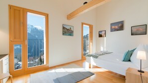 A bedroom with a bed, a nightstand, a lamp, and a view of mountains through large windows.