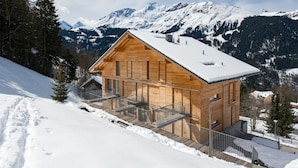 A wooden cabin with a balcony, surrounded by snow-covered mountains.