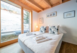 A bedroom with a large bed, a window with a view of a snowy landscape, and artwork on the wall. - Chalet Roossi Penthouse (Wengen)