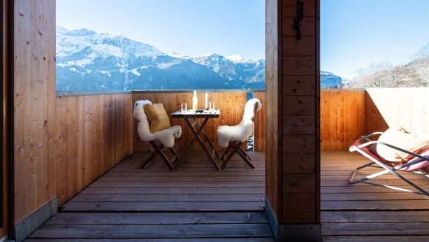 A wooden deck with a table and two chairs, overlooking a snowy mountain range.
