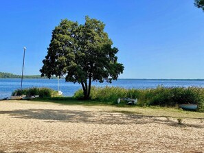 A sandy beach with boats, a tree, and a clear blue sky. - Cottage with an idyllic garden at the lake G0239 (Lacanau)