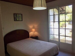A bedroom with a bed, a nightstand, a lamp, a picture on the wall, and a window with a view of the outdoors.