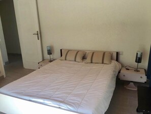 Ein Einzelzimmer mit einem Bett, einer weißen Bettdecke, zwei Nachttischlampen und einem Nachttisch.
