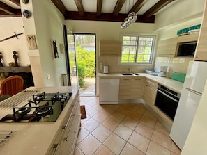 A kitchen with a gas stove, dishwasher, oven, and a window overlooking greenery. - Cottage with an idyllic garden at the lake G0239 (Lacanau)