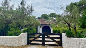 A gated entrance with a stone wall and a small building with a tiled roof. - Renovated landaise style house with enchanted garden, 2 steps from the lake (Lacanau)