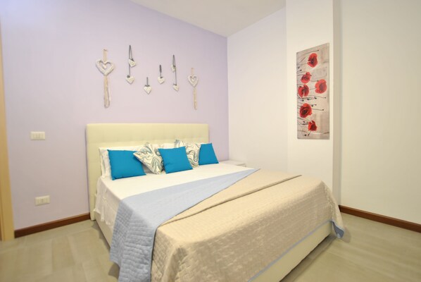 A bedroom with a bed, pillows, a wall art piece, and a light switch. - Smeralda Flats, 2 bedroom & parking historic center (Olbia)