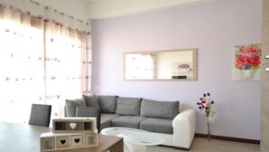 Ein modernes Wohnzimmer mit einem grauen Sofa, einem Glastisch und einem weißen Sessel. Ein Holztisch mit herzförmigen Ausschnitten ist sichtbar.