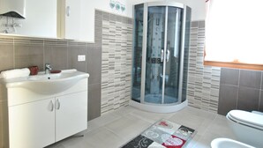 Ein modernes Badezimmer mit einer gläsernen Duschkabine, einem weißen Waschbecken mit roter Schüssel und einem gemusterten Teppich auf dem Boden.