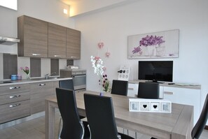 A modern kitchen with built-in appliances, a dining area with a table and chairs, and a TV mounted on the wall. - Smeralda Flats, 2 bedroom & parking historic center (Olbia)