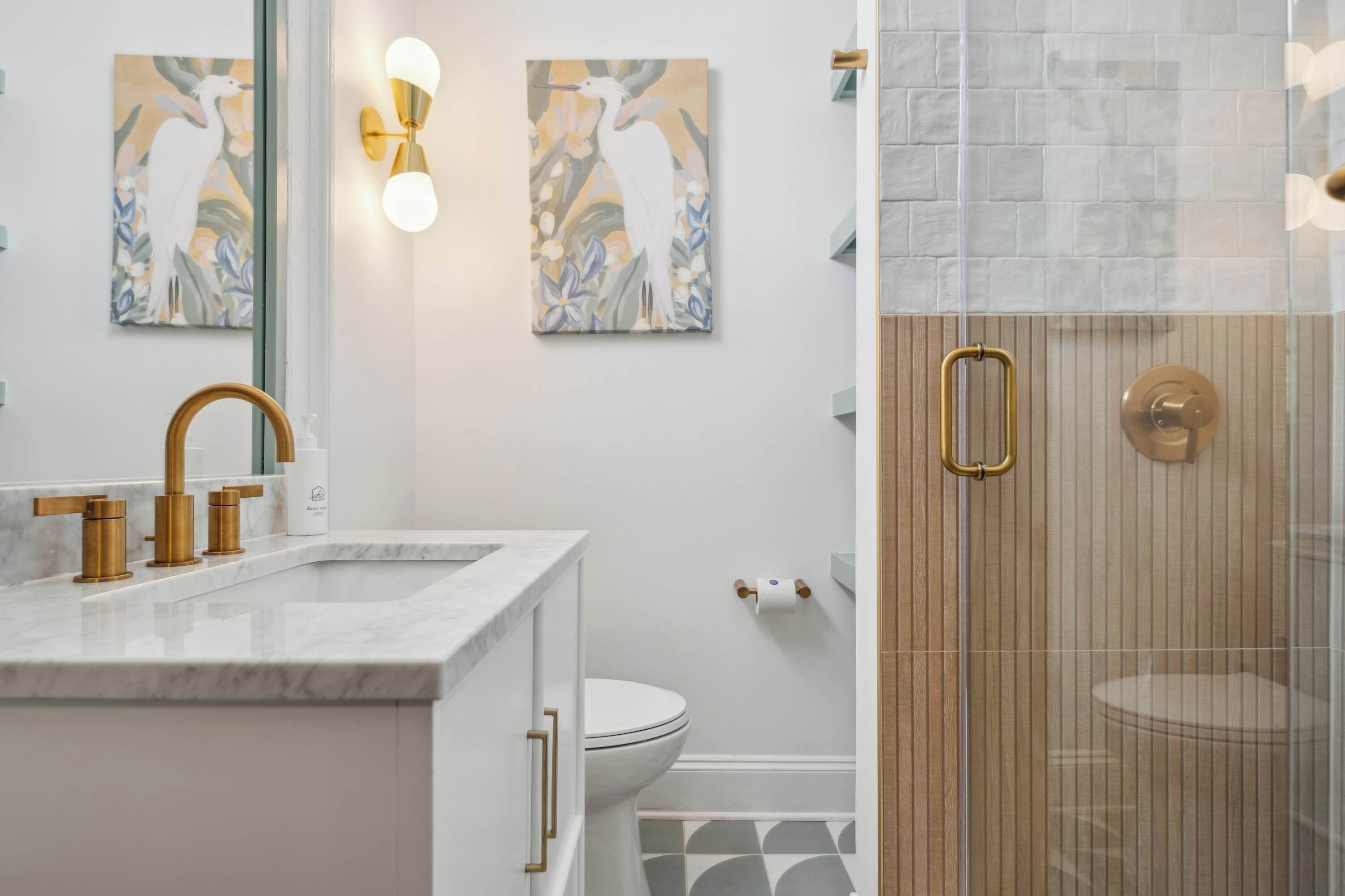 Une salle de bain moderne avec un lavabo en marbre, des robinetteries dorées et deux tableaux accrochés au mur.