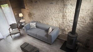 Una sala de estar acogedora con un sofá gris, una silla de madera, una mesita con una lámpara y un estufa de leña.