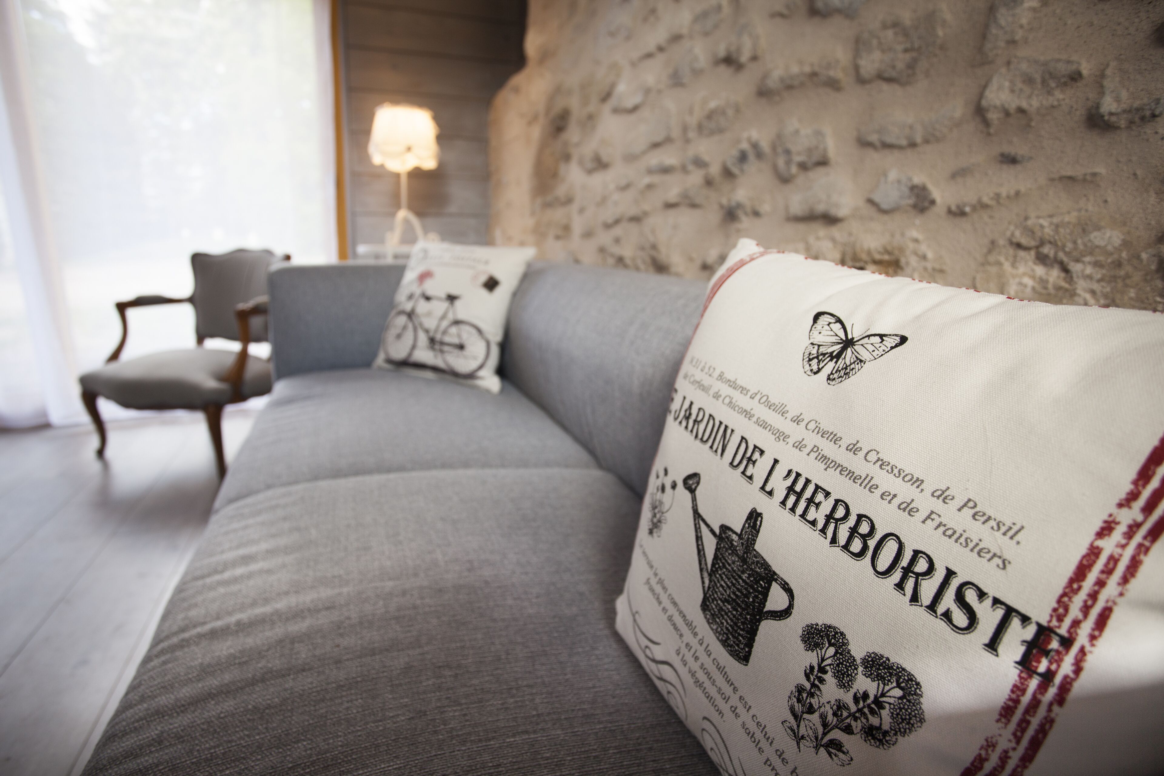 Ein modernes Wohnzimmer mit einem grauen Sofa, einem dekorativen Kissen mit Text, einer Lampe und einem Sessel.