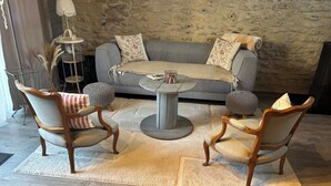 Una sala de estar acogedora con un sofá gris, dos sillas de madera, una mesa de centro redonda y una pared de piedra.