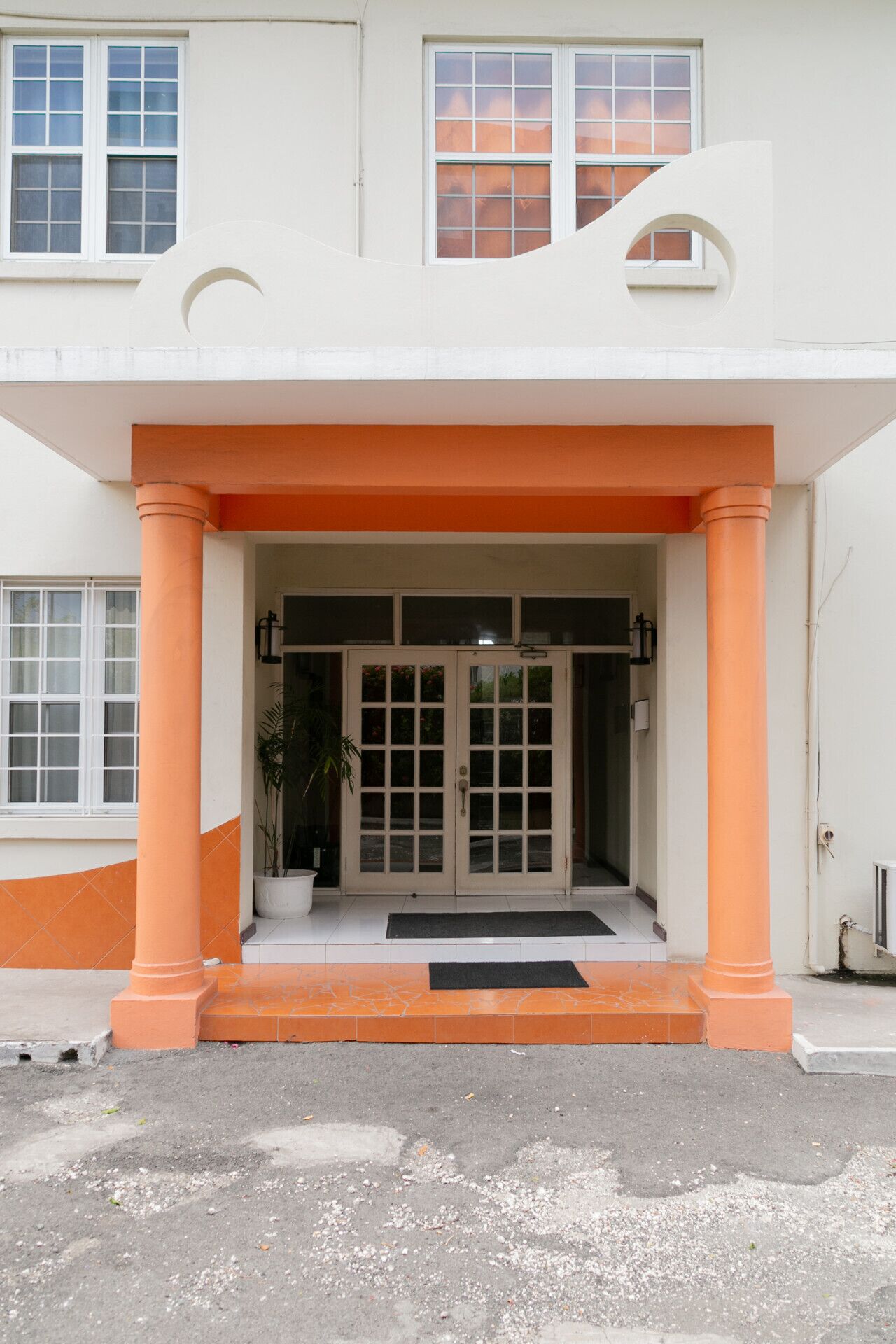 Un bâtiment à la façade blanche, agrémenté de touches de couleur orange, et doté d’une entrée centrale avec un double portail.
