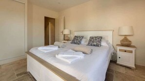 A neatly made bed with white linens and two pillows, a bedside table with a lamp, and a door to the left.