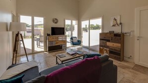 A spacious living room with a sofa, coffee table, and a TV. There is a sliding glass door leading to an outdoor area.