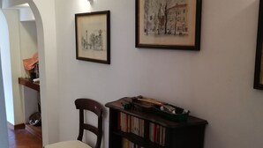 A hallway with a wooden chair, a bookshelf, and two framed pictures on the wall. - Talents Home Historical center (Lucca)