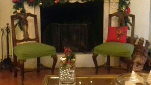 A cozy living room with a fireplace, two green upholstered chairs, and a glass coffee table with a decorative vase. - Talents Home Historical center (Lucca)