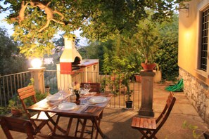 An outdoor dining area with a wooden table set for two, surrounded by potted plants and a stone wall. - Terrace On the Park - "Carretteria" (modica)