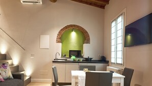 A modern kitchen with a dining area, wooden ceiling beams, and a TV mounted on the wall. - "GIADA" - Elegant Penthouse for 4 people on the 3rd floor on 2 levels (Firenze)