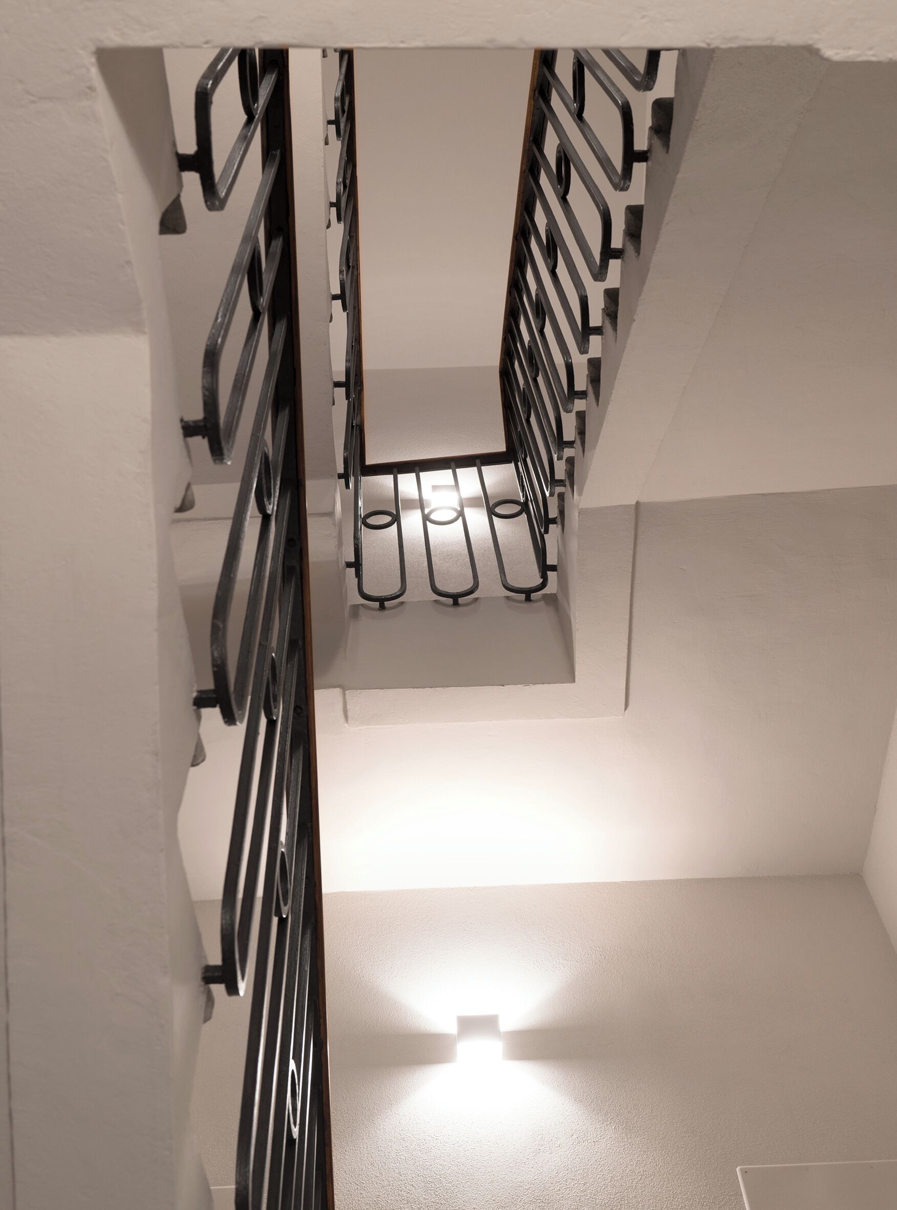 A narrow, enclosed stairwell with metal railings and a light source at the bottom.