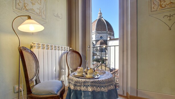 A dining area with a table set for two, a chair, a lamp, and a view of a historic building. - Central apartment for visiting Florence (Firenze)