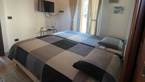 Une chambre avec un grand lit, un téléviseur à écran plat fixé au mur et une fenêtre avec des rideaux.