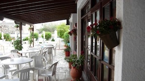 Ein Patio im Freien mit weißen Plastikstühlen und -tischen, Blumentöpfen und hängenden Blumenkörben.