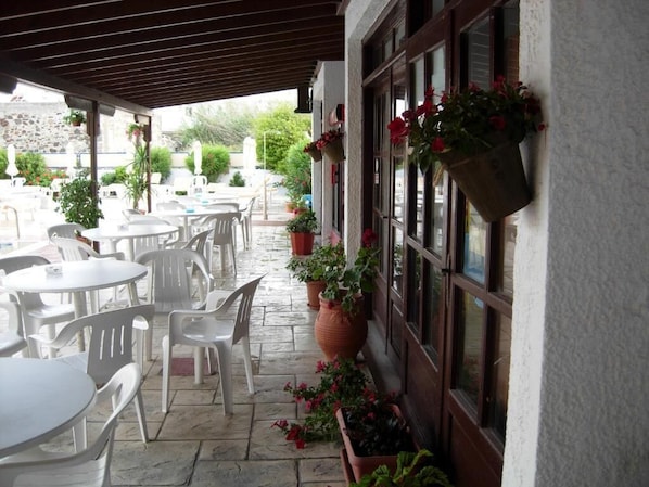 An outdoor patio area with white plastic chairs and tables, potted plants, and hanging flower baskets.