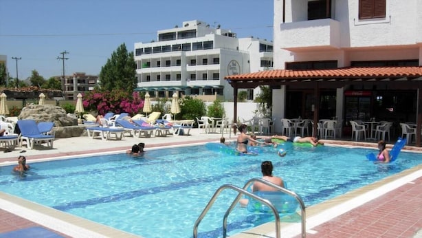 Ein Schwimmbecken mit Liegestühlen und Sonnenschirmen, umgeben von Gebäuden und einer Bar.