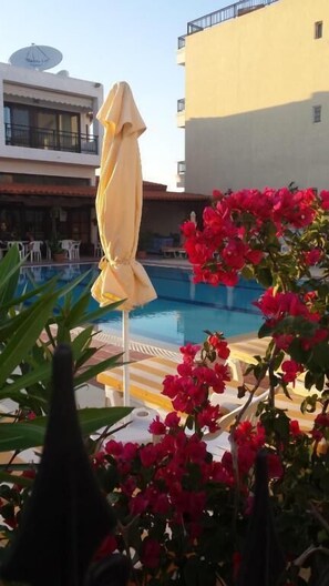 A swimming pool with a yellow umbrella, surrounded by red flowers and a building with balconies.