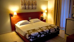 Ein Hotelzimmer mit einem großen Bett, zwei Nachttischlampen, einer Wandklimaanlage, einem kleinen Tisch mit einer Pflanze und einem Schreibtisch mit einem Wasserkocher.