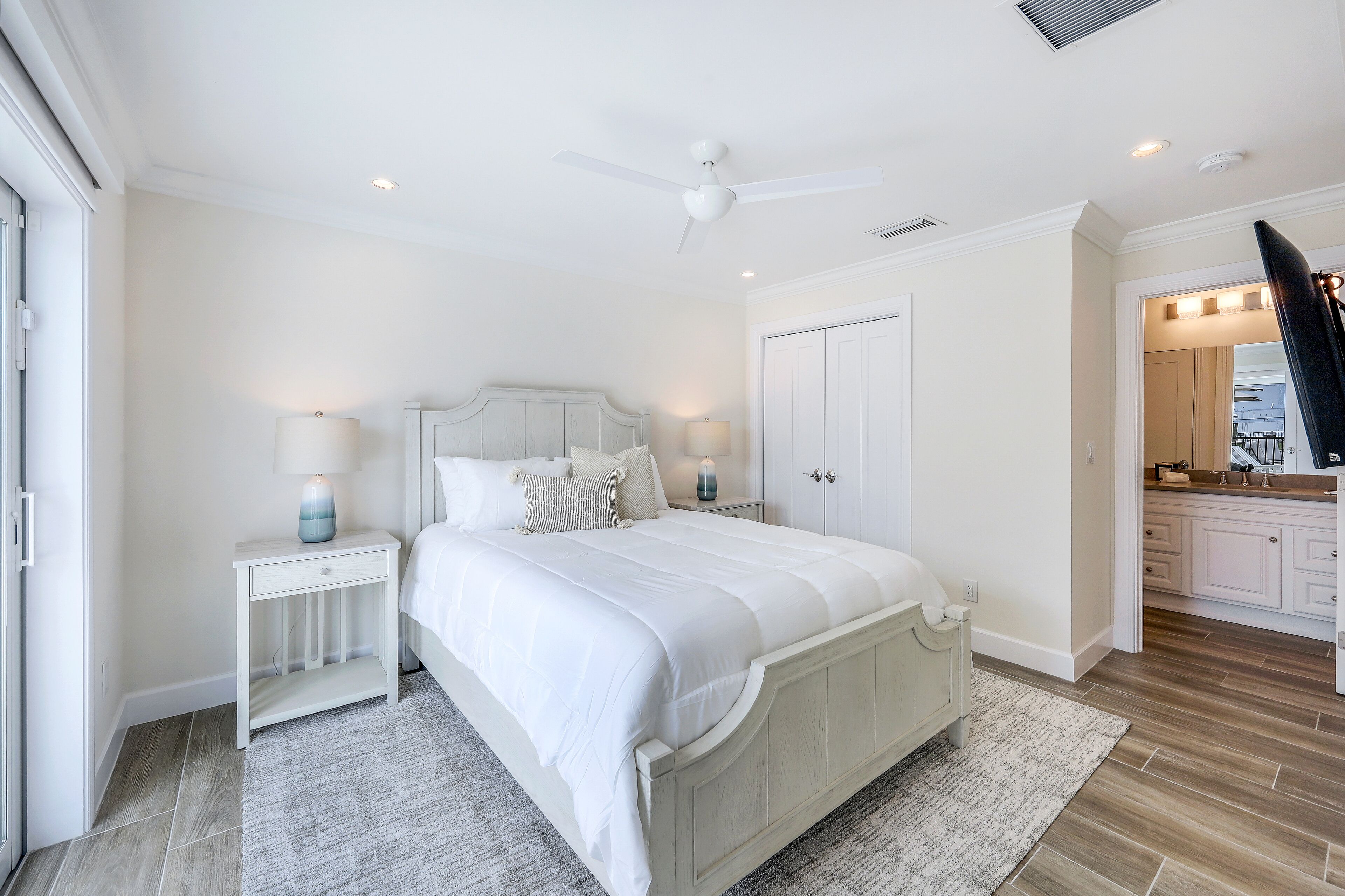 A bedroom with a bed, nightstands, a ceiling fan, and a view into the adjacent bathroom.