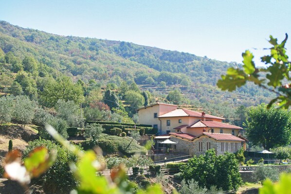 A two-story building with a red-tiled roof, surrounded by lush greenery and hills.