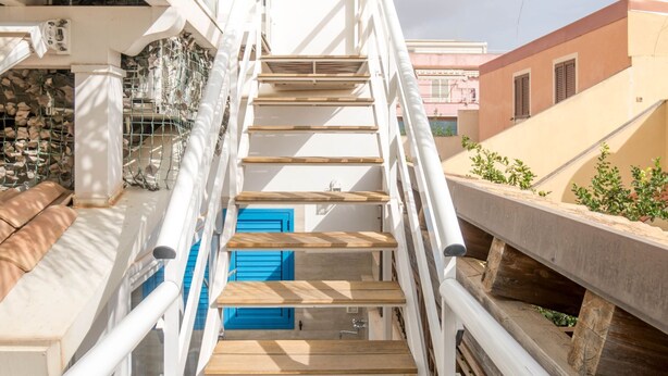 Eine Treppe mit Holzdielen und weißen Geländern, die zu einem Balkon mit blauen Fensterläden führt.