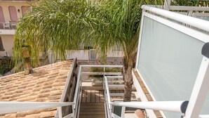Eine Holztreppe führt zu einem Balkon mit Blick auf Häuser mit Terrakotta-Dächern und einer Palme.